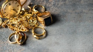 Schmuck und alte Goldstücke, darunter Ringe, Ketten und eine Uhr auf dunkler Oberfläche.